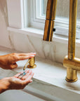Person washing hands under a BRASS faucet in a bathroom.