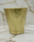 Hammered brass textured wastebasket on a marble surface with a neutral background