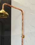 Gold shower head attached to a copper pipe against a tiled wall.