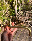 Person holding a vintage brass faucet outdoors with a wicker chair and greenery in the background.