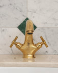 Gold faucet on a tiled wall with green and white diamond pattern