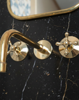 Brass bathroom faucet and handles on a black marble wall