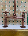 Copper kitchen faucet against a tiled wall with green and beige tiles.