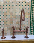 Copper kitchen faucet set against a mosaic tile wall with green and beige tiles.