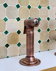 Copper faucet against a tiled wall with green and beige tiles