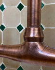Close-up of a copper faucet handle against a tiled wall background