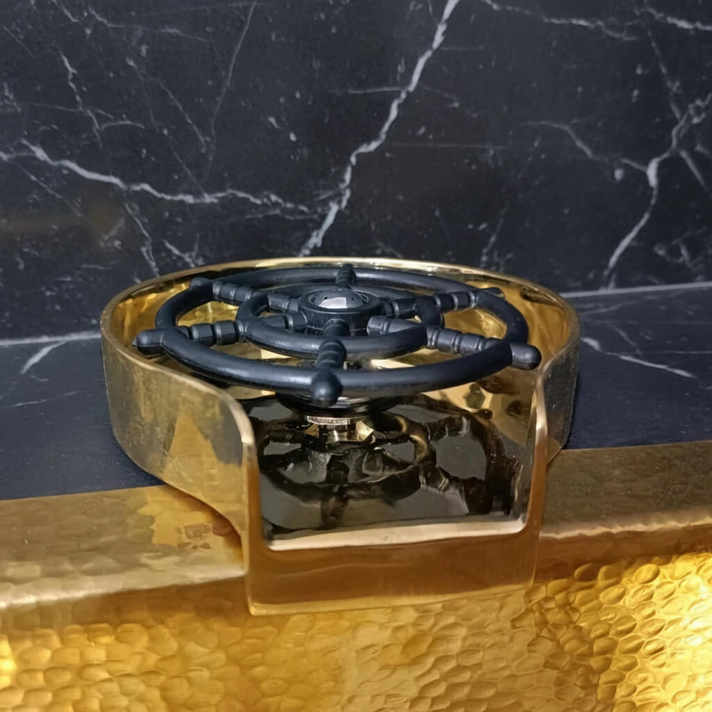 Brass Glass Rinser object with black central design on a marble surface