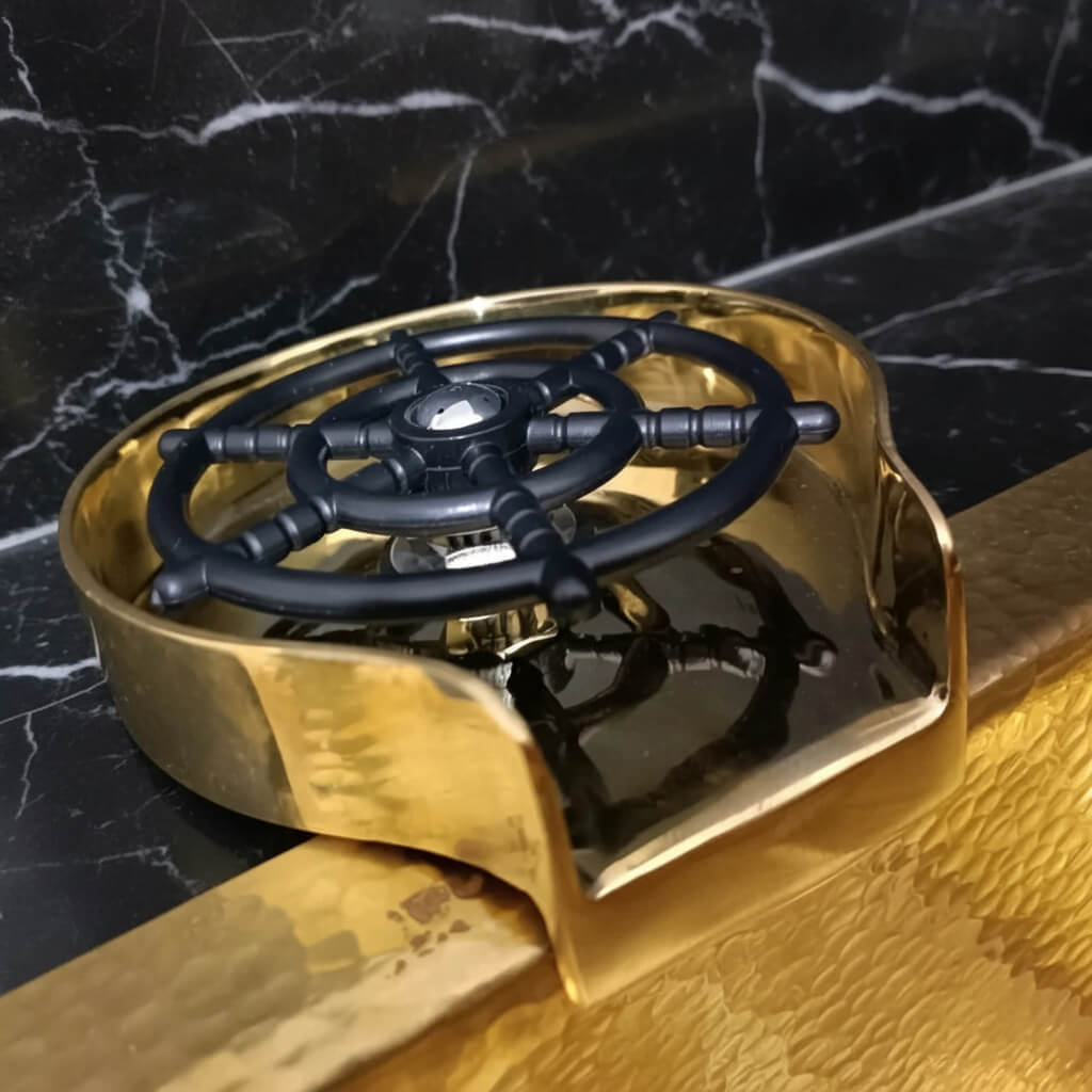 Brass Glass Rinser object with black central design on a marble surface