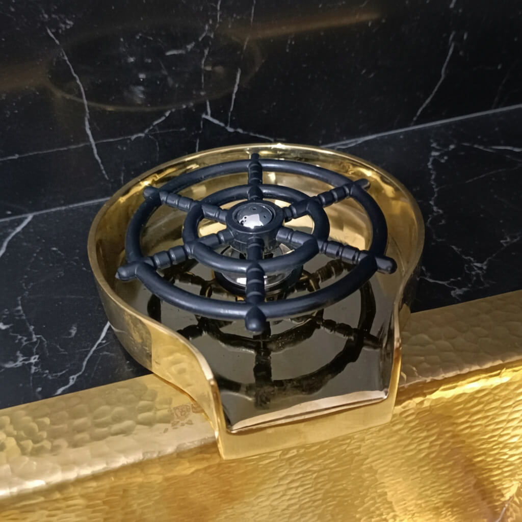 Brass Glass Rinser object with black central design on a marble surface