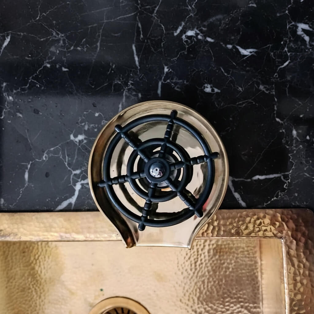 Brass Glass Rinser object with black central design on a marble surface