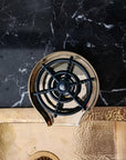 Brass Glass Rinser object with black central design on a marble surface