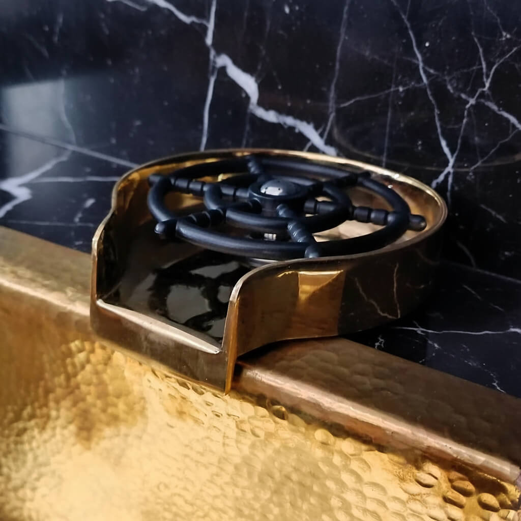 Brass Glass Rinser object with black central design on a marble surface