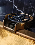 Brass Glass Rinser object with black central design on a marble surface