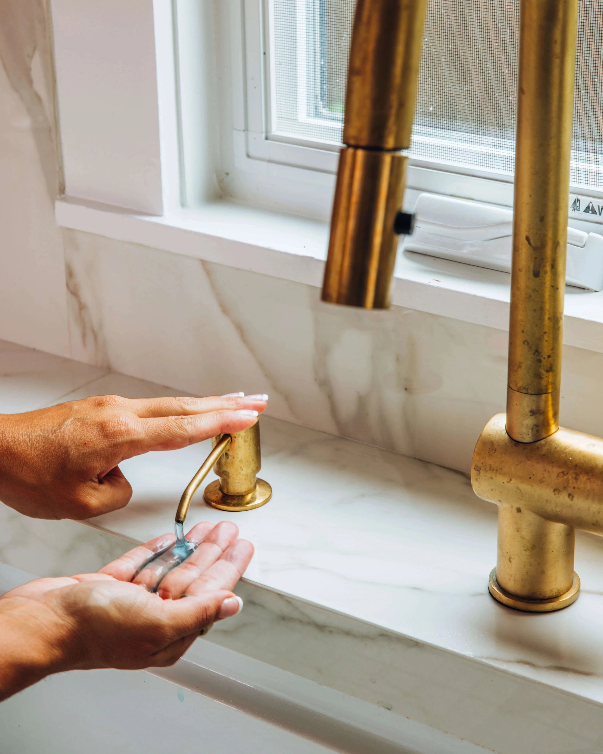 Person washing hands under a BRASS faucet in a bathroom.