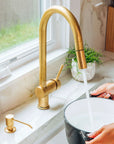 Brass kitchen faucet with running water into a black pot on a white countertop.
