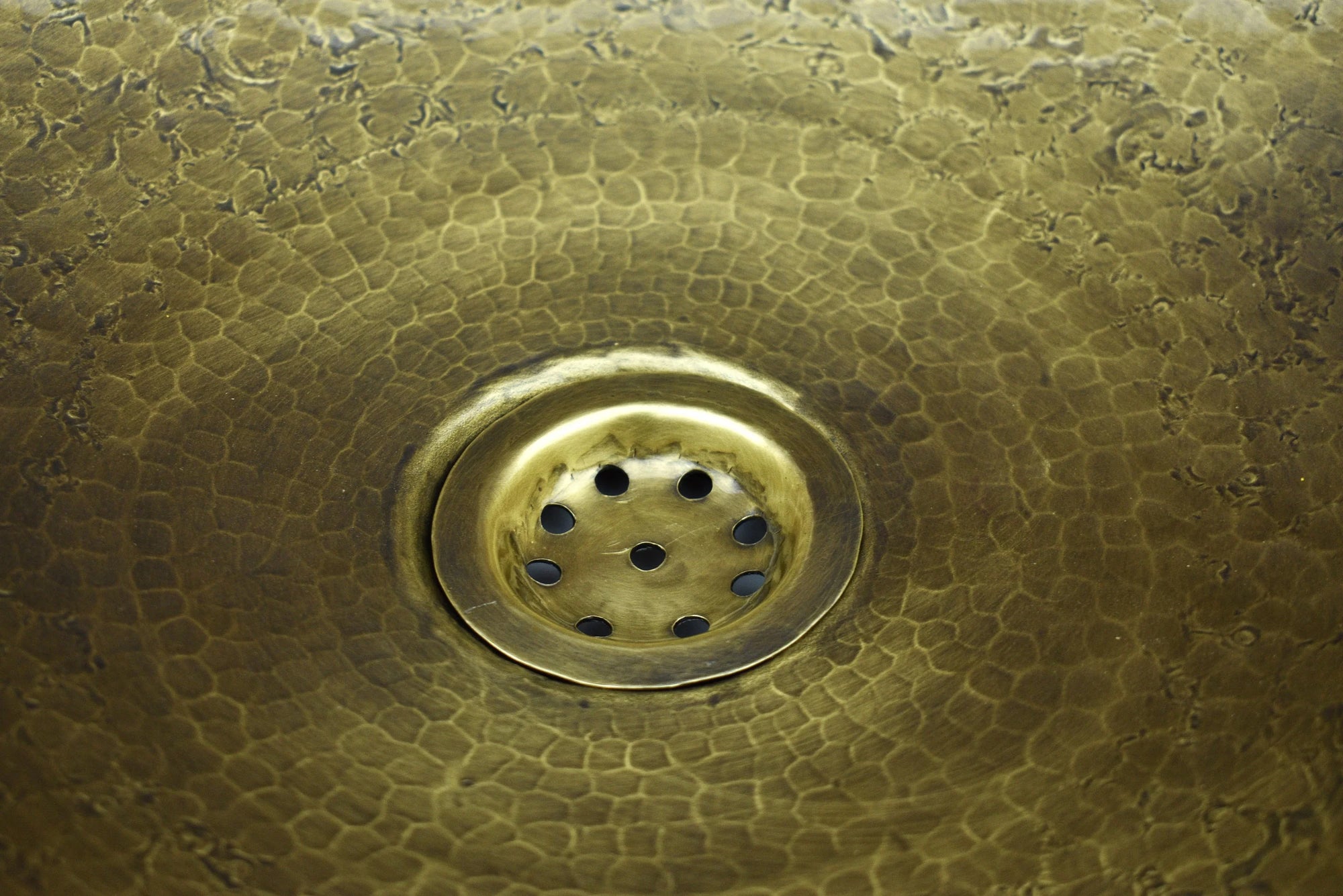 Close-up of a brass drain cover on a textured Bronze drop in sink
