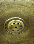 Close-up of a brass drain cover on a textured Bronze drop in sink
