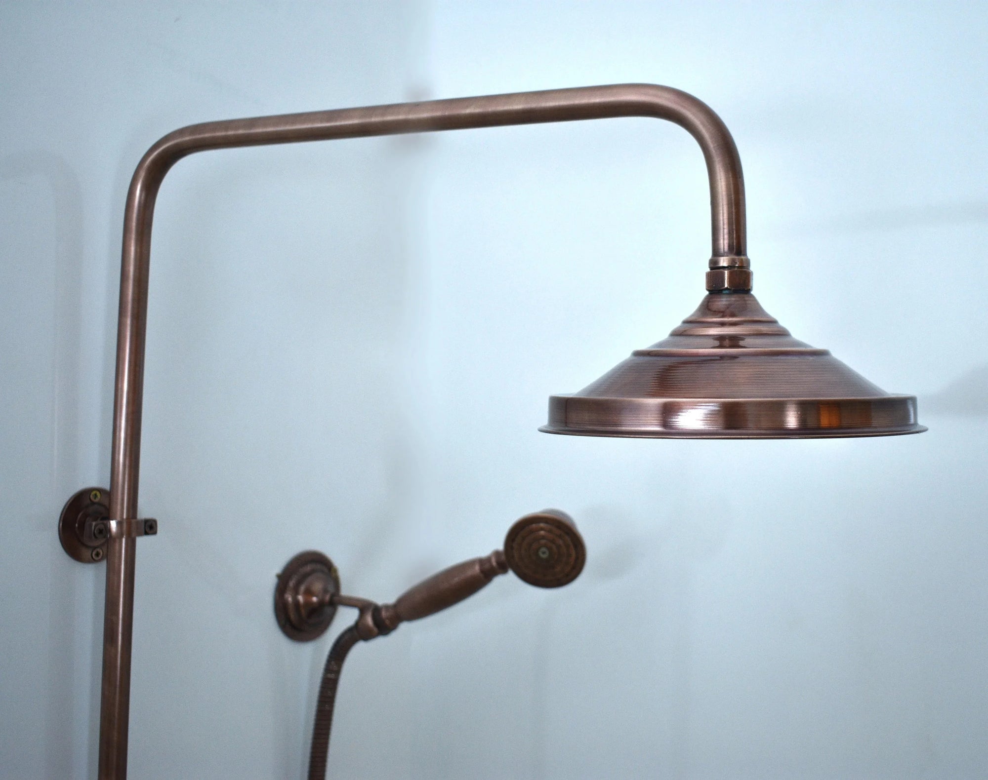 Vintage-style copper shower head and arm against a light blue background