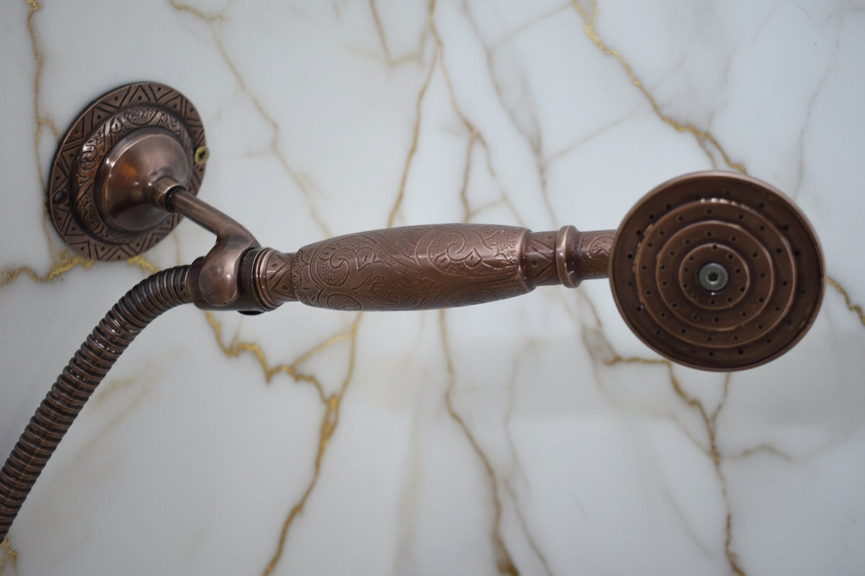 Vintage-style copper shower head and hose against a light blue background