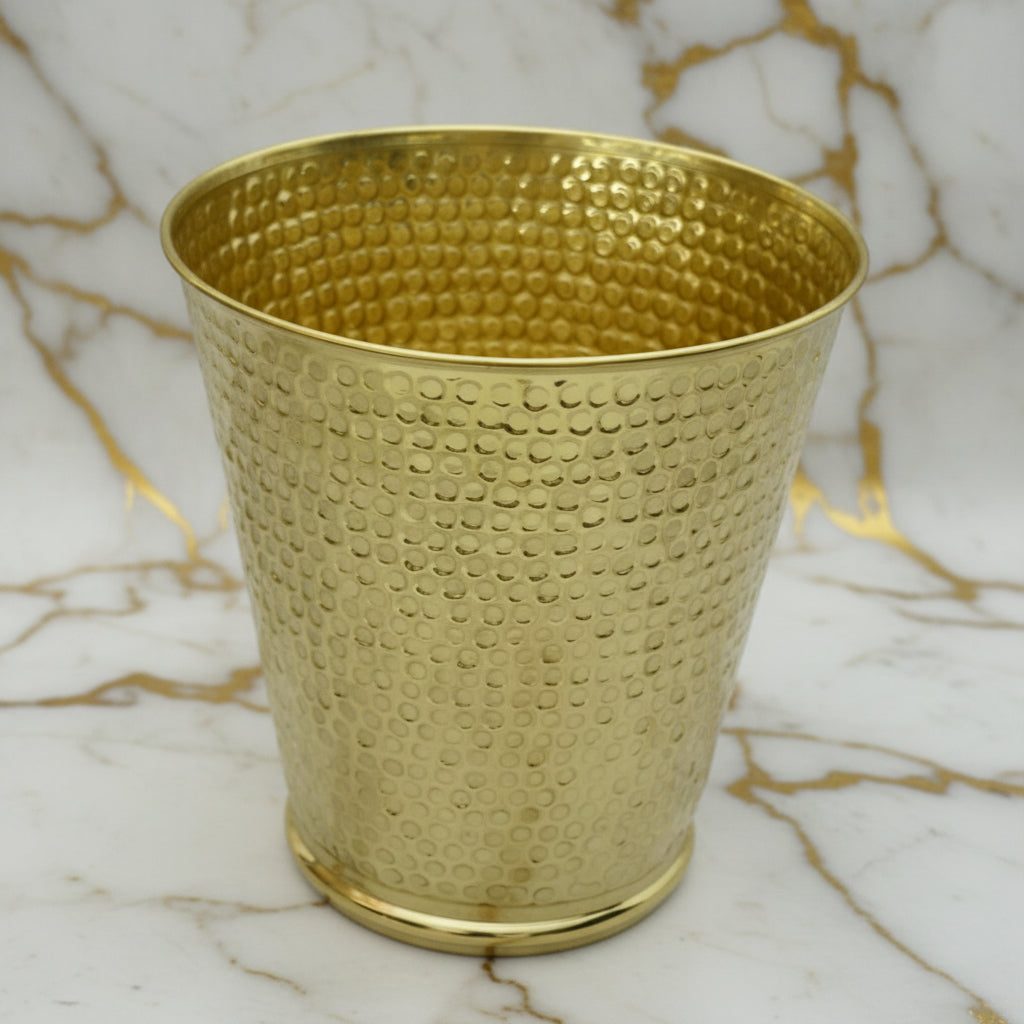 Hammered brass textured wastebasket on a marble surface with a neutral background
