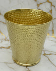 Hammered brass textured wastebasket on a marble surface with a neutral background