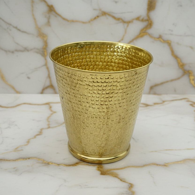 Hammered brass textured wastebasket on a marble surface with a neutral background