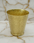 Hammered brass textured wastebasket on a marble surface with a neutral background