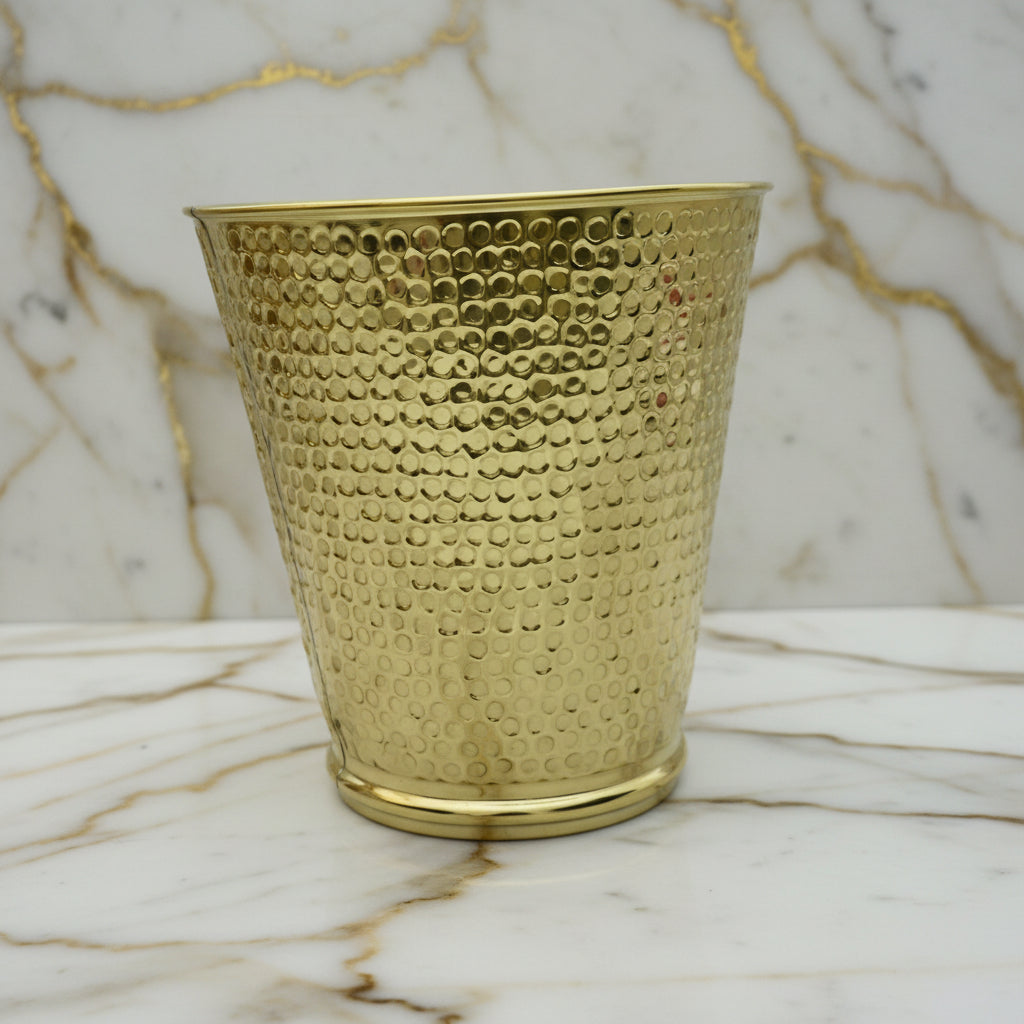 Hammered brass textured wastebasket on a marble surface with a neutral background