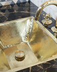 Brass sink with a gold faucet on a dark marble countertop