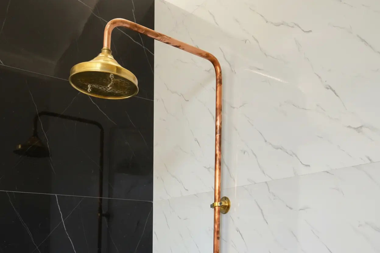 Gold shower head attached to a copper pipe against a tiled wall.