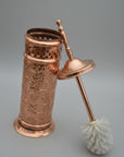Copper toilet brush holder with intricate designs on a dark surface.