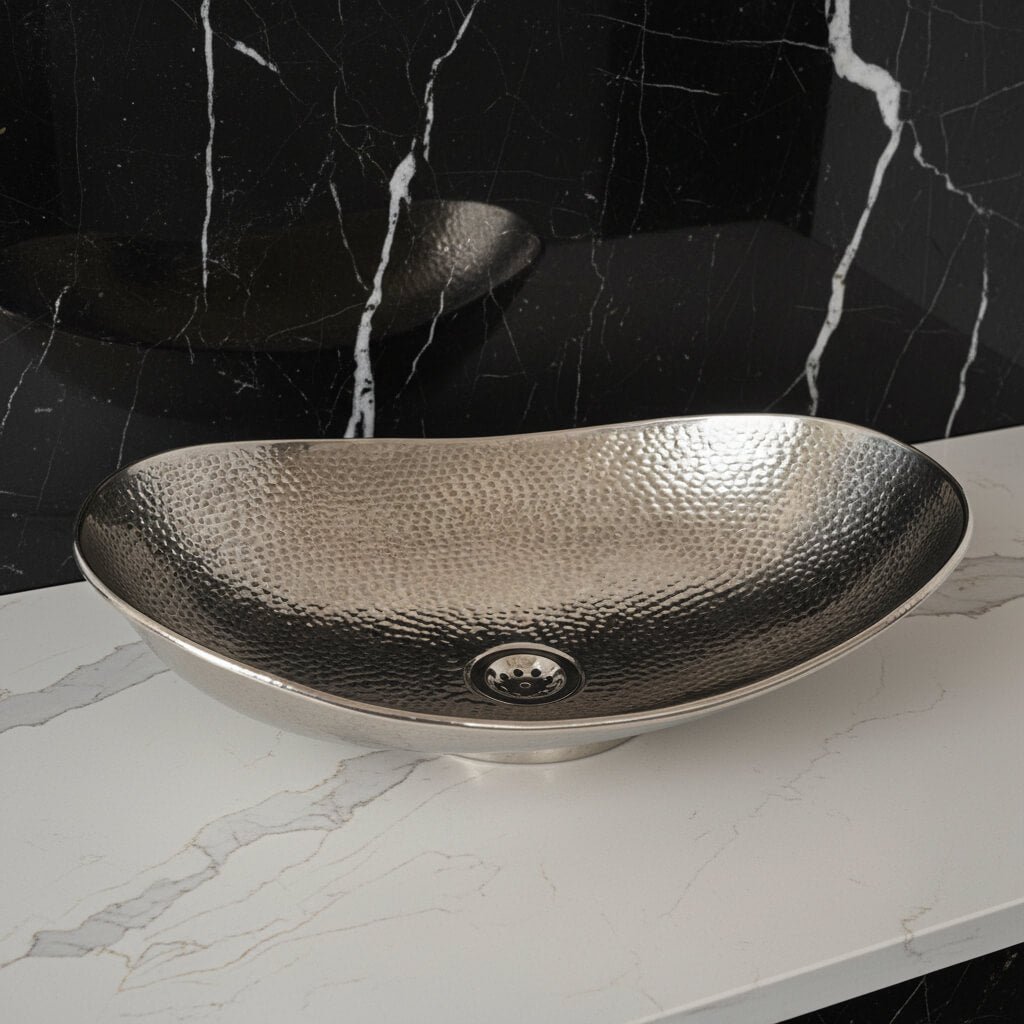 Hammered metal sink on a marble countertop with a black marble wall background