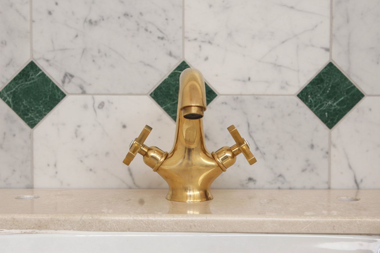 Gold faucet on a tiled wall with green and white diamond pattern