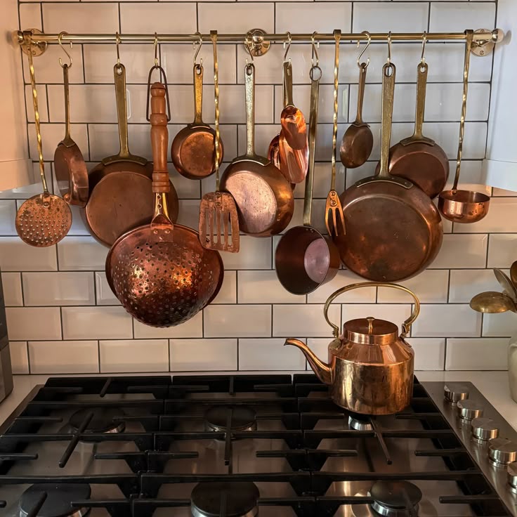 Collection of copper pots and pans hanging above a stove with a tiled wall background.