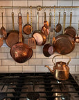Collection of copper pots and pans hanging above a stove with a tiled wall background.