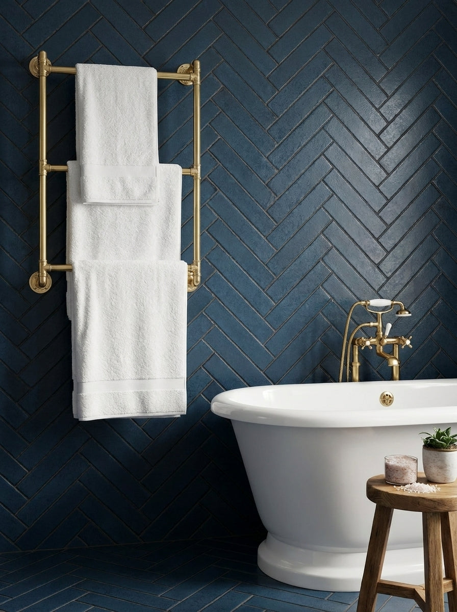 Bathroom with white towels on a gold towel rack against a blueherringbone-patterned wall.