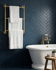 Bathroom with white towels on a gold towel rack against a blueherringbone-patterned wall.