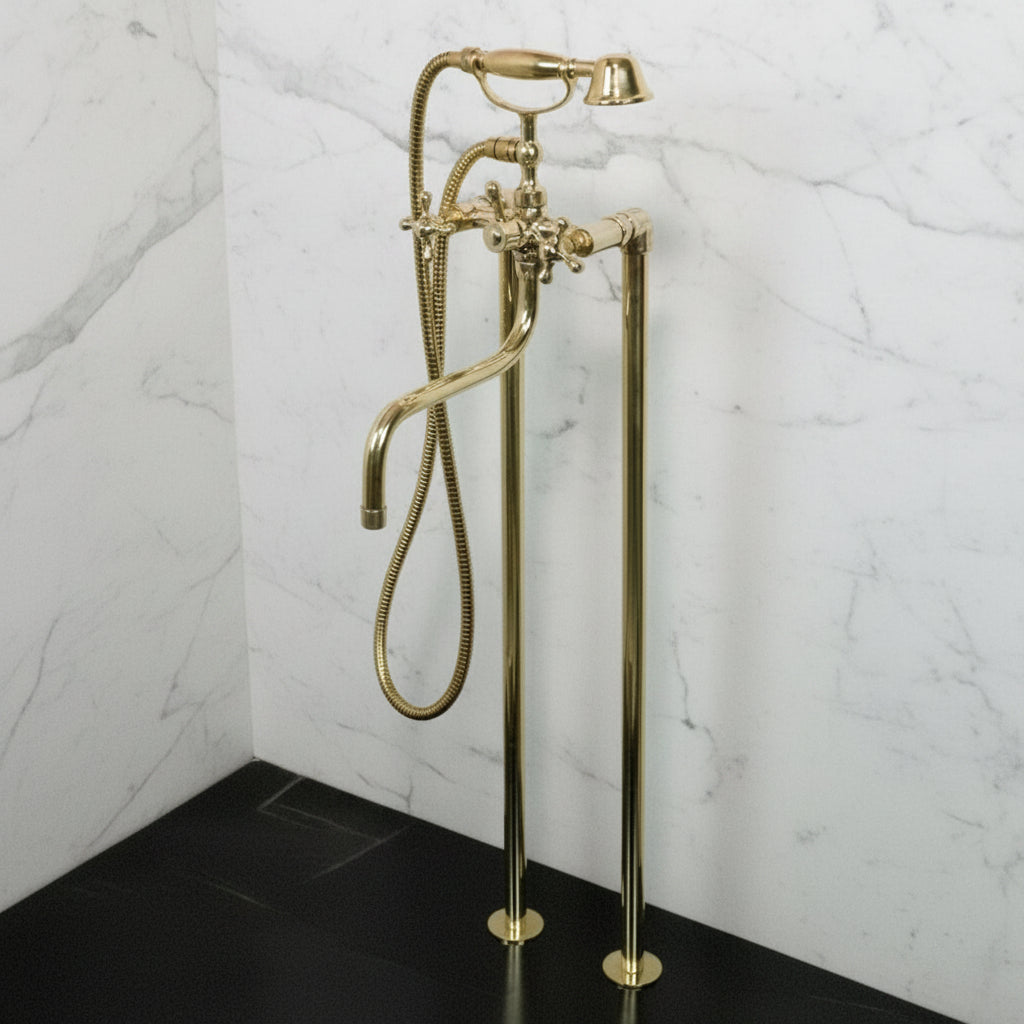 Brass freestanding bathtub faucet with handheld shower head against a white wall.