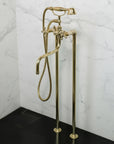 Brass freestanding bathtub faucet with handheld shower head against a white wall.