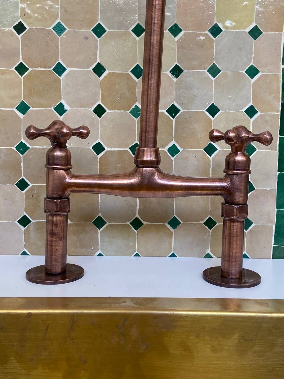 Copper kitchen faucet against a tiled wall with green and beige tiles.