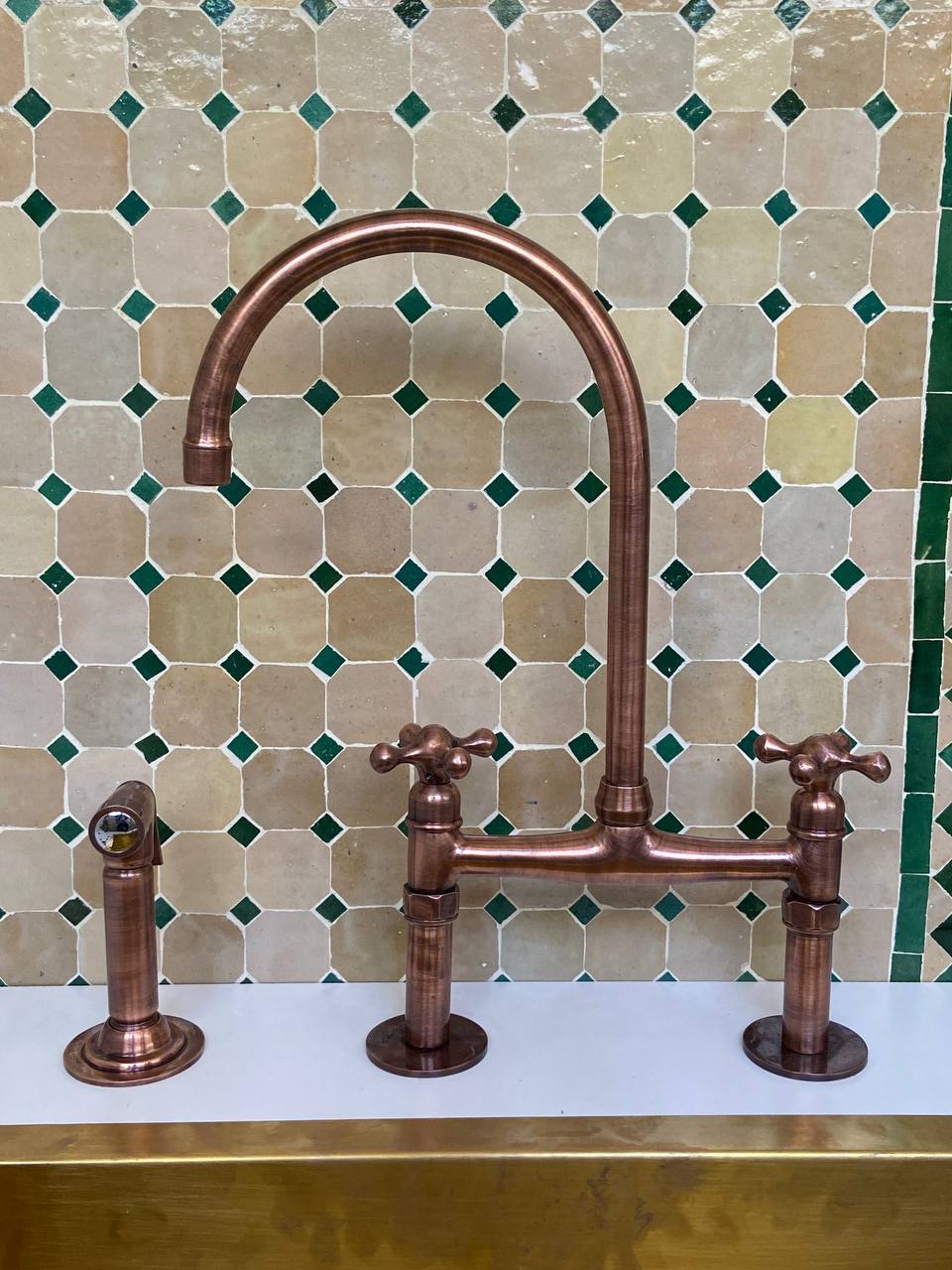 Bronze kitchen faucet with two handles against a mosaic tile backsplash.