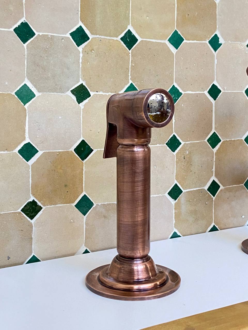 Copper faucet against a tiled wall with green and beige tiles
