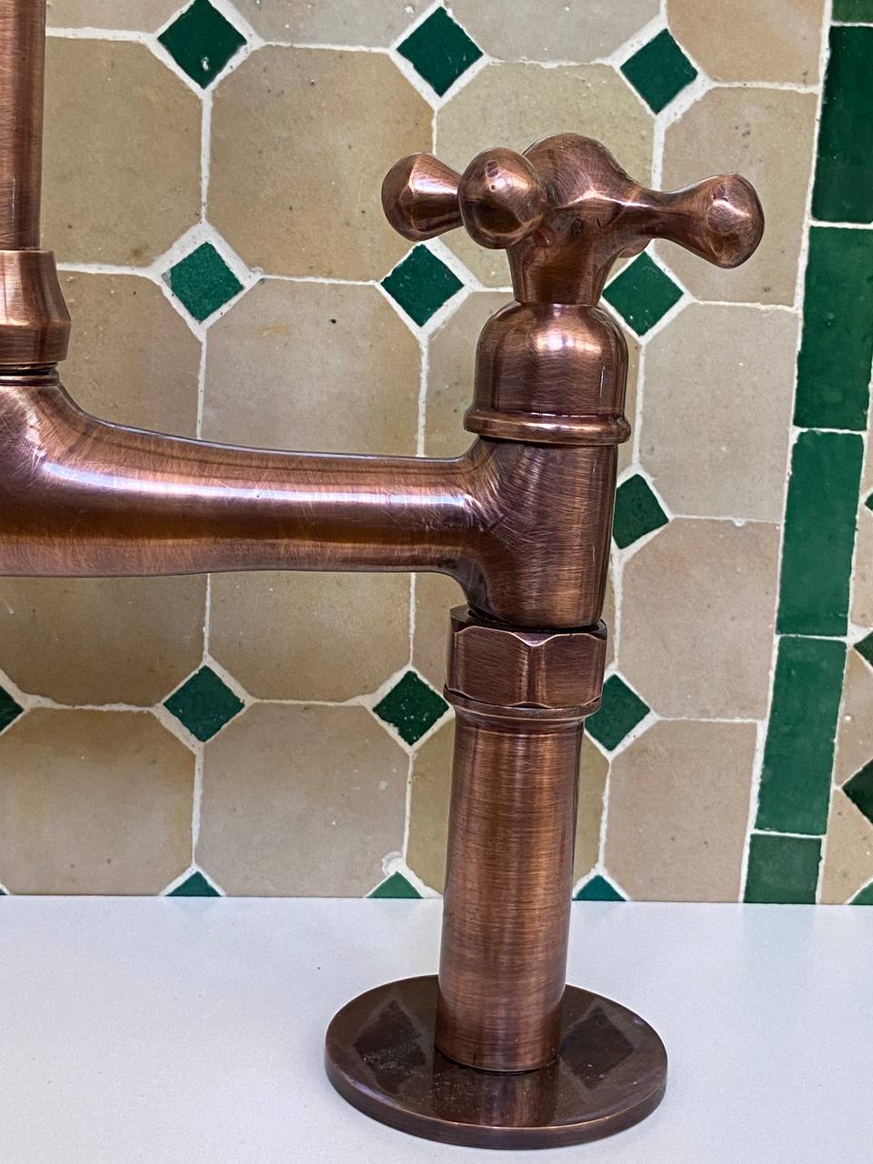 Copper faucet against a tiled wall with green and beige tiles