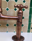 Copper faucet against a tiled wall with green and beige tiles