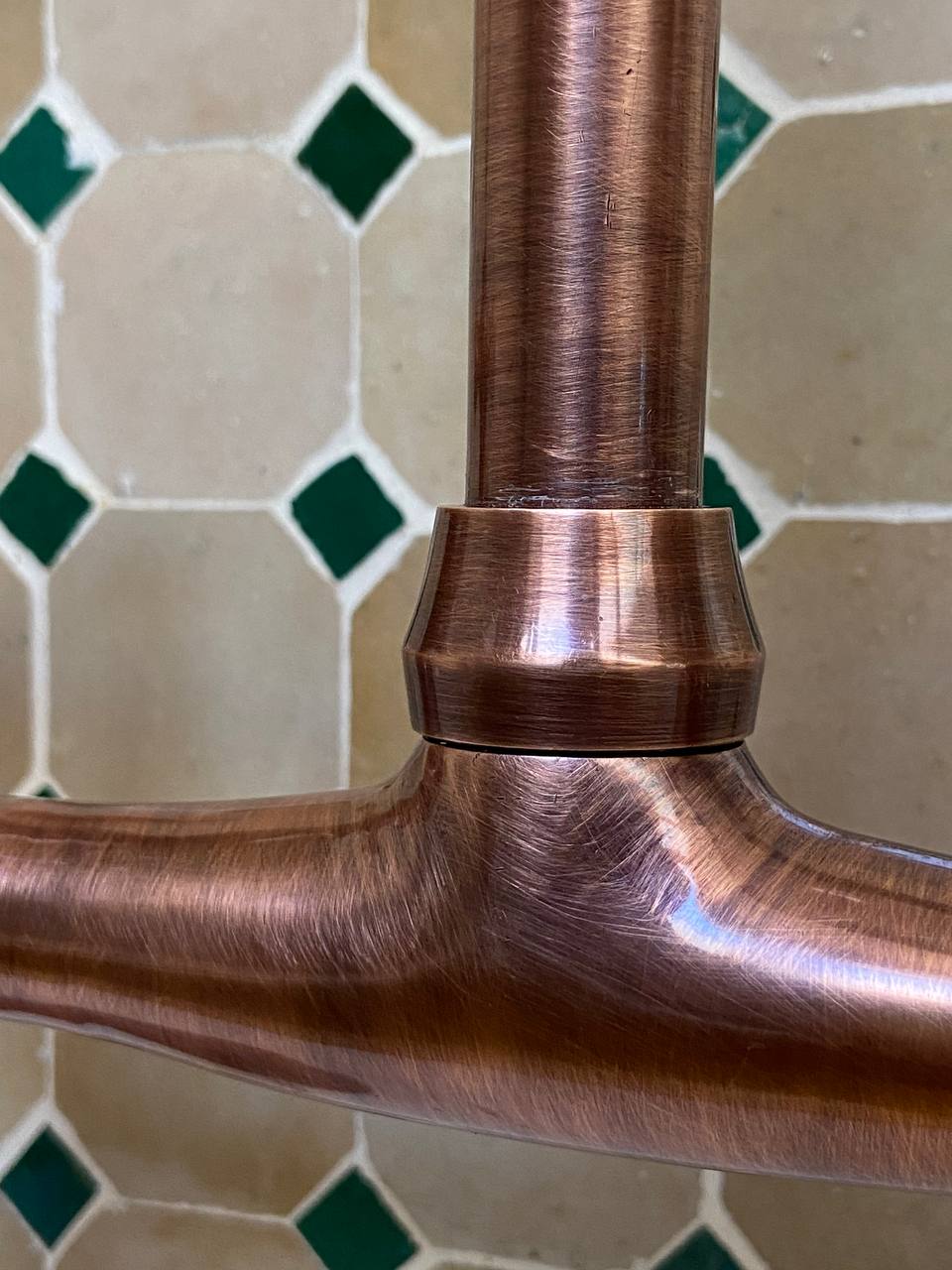 Close-up of a copper faucet handle against a tiled wall background