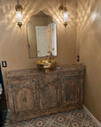 Bathroom with wooden vanity, gold sink, and decorative mirror.